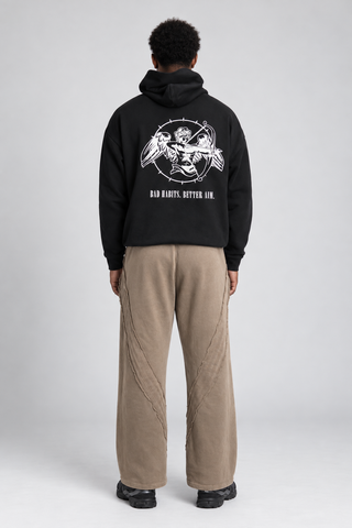 Back full-body studio view of a model wearing the Black Bad Habits Hoodie, showing the cupid archer graphic and BAD HABITS. BETTER AIM. text.