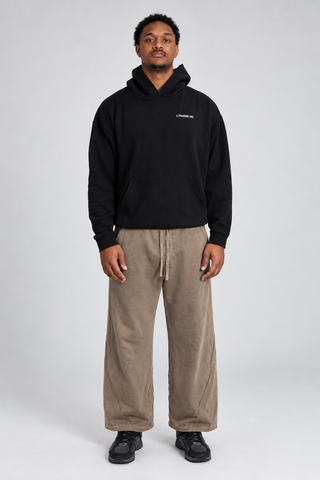 Front full-body studio view of a model wearing the Black Bad Habits Hoodie with taupe wide-leg pants and black sneakers.
