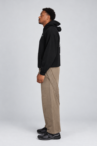 Side-profile full-body studio view of a model wearing the Black Bad Habits Hoodie, showing the hood, sleeve, body length, and outfit silhouette.