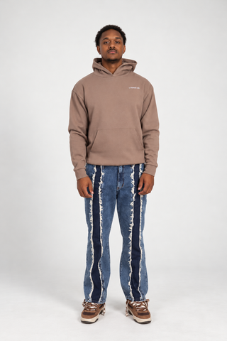 Front full-body studio view of a model wearing the Clay Bad Habits Hoodie with distressed panel jeans and brown sneakers.