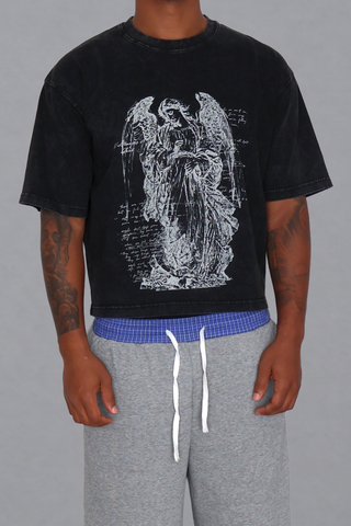 Front view of a model wearing the black washed Guardian Cropped T-Shirt, showing the angel graphic, boxy fit, and cropped hem.