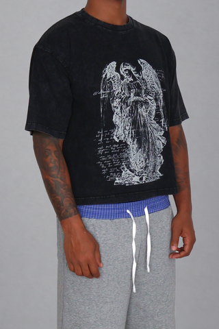 Right three-quarter view of a model wearing the black washed Guardian Cropped T-Shirt, showing the angel graphic, sleeve volume, and cropped fit.