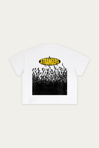A white short-sleeve t-shirt shown flat against a light beige background, featuring a graphic print on the back with a yellow 'STRANGERS' logo above a black-and-white crowd illustration.