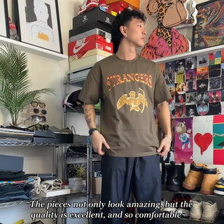 Person wearing a brown 'Strangers' t-shirt in a room