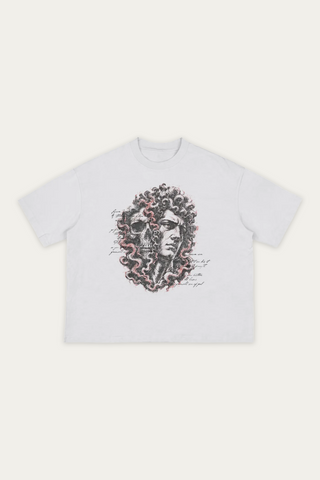 A white short-sleeve crewneck t-shirt featuring a graphic print of a male's face on the right & a partial skull face appearing from black, grey, and pink smoke wrapped all around and between the heads, displayed flat against a light off-white background.