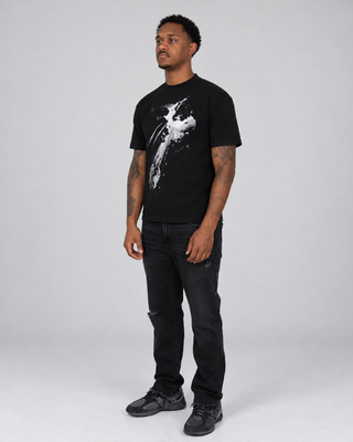 Full-body left three-quarter view of a model wearing the black Fallen T-Shirt with black jeans and dark sneakers.