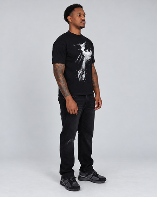 Full-body right three-quarter view of a model wearing the black Fallen T-Shirt with black jeans and dark sneakers.