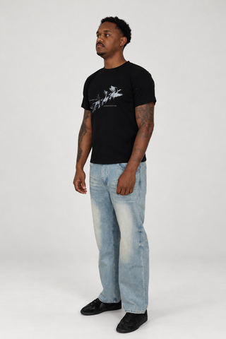 Model wearing the black Somewhere Better T-Shirt and light blue Sun Fade Raw Hem Jeans, full-body left three-quarter studio view.