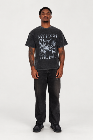 Front view of a model wearing The Fall T-Shirt in Black Washed with black jeans and dark sneakers in a light studio.